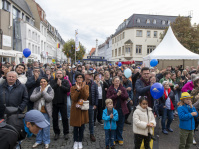Menschenmenge in der Innenstadt von Saarbrücken klatscht bei einer Veranstaltung, Luftballons in Blau und Gelb sichtbar.