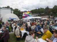 Menschen sitzen an Tischen vor einem weißen Thüringen-Zelt mit großer Kuppel und buntem Wandbild.