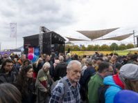 Menschenmenge vor einer Bühne mit schwarzem Pavillon und bunten Luftballons.