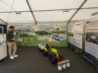 Mann demonstriert ferngesteuertes Modell eines Traktors im Zelt mit Informationswänden zu KI in der Landwirtschaft.