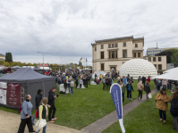 Menschenmenge auf einer Wiese mit weißen Zelten und einer großen weißen Kuppel vor einem historischen Gebäude.