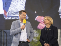 Ein Mann mit Mikrofon und eine Frau stehen auf einer Bühne 