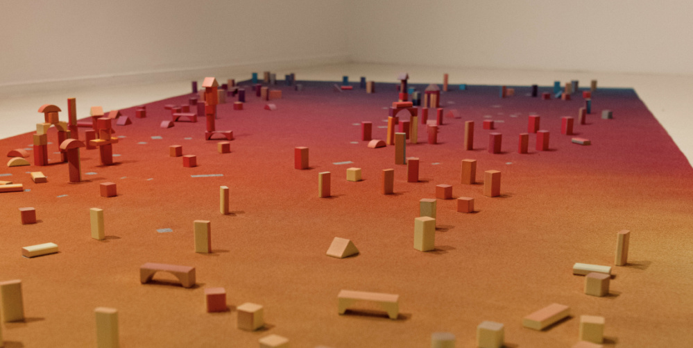 Zu sehen ist ein bunter Teppich mit Holzblöcken, es handelt sich um das Kunstwerk PLAYGROUND von Vanessa Husson &  Geoffrey Blan. 