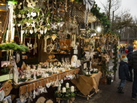 Ein reich dekorierter Stand voller Holz- und Naturdekorationen, Kerzen und Hängeschmuck; Besucher laufen daran vorbei.