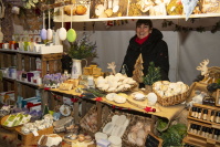 Eine Verkäuferin steht hinter einem Stand voller Naturseifen, Badeprodukte und kleinen Geschenkartikeln, dekoriert mit Tannengrün und weihnachtlichen Elementen.