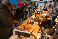 Besucherinnen und Besucher schauen bei Regen und unter Regenschirmen an einem Marktstand mit bunten Keramik-Weihnachtsfiguren vorbei.
