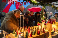 Besucherinnen und Besucher schauen bei Regen und unter Regenschirmen an einem Marktstand mit bunten Keramik-Weihnachtsfiguren vorbei.
