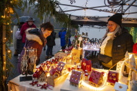 Erleuchteter Stand mit Häusern und Lichterketten, eine Frau begutachtet Waren. 
