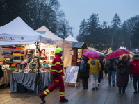 Ein breiter Marktweg mit vielen Menschen unter bunten Regenschirmen, flankiert von Ständen mit Filzprodukten und anderen Waren; es ist nass und dämmrig.