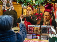 Zwei Frauen bedienen an einem weihnachtlich geschmückten Verkaufsstand mit Süßwaren.