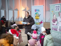 Eine Frau führt lachende Kinder vor einer bunt dekorierten Bühne mit Sing-Glöckchen-Bannern.