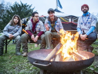 Pfadfinder sitzen entspannt am Lagerfeuer vor einer Jurte und wärmen sich im Abendlicht.
