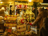 Ein beleuchteter Marktstand mit Seifen, Deko und Holzkunst, den Besucher neugierig betrachten.