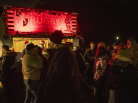 Eine Menschenmenge steht vor einem rot beleuchteten Rugby-Stand und genießt warme Getränke.