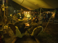 Besucher wärmen sich an einem Feuer unter einem großen mittelalterlichen Zeltdach, während Kinder zuschauen.