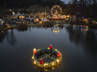 Ein schwimmender Adventskranz leuchtet auf dem Weiher, dahinter Marktstände und ein Riesenrad.
