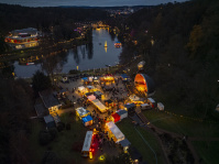 Blick von oben auf die Bühne und zahlreiche Marktstände, dahinter der hell beleuchtete Weiher.
