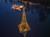 Ein beleuchteter Lichterbaum treibt auf dem Weiher, während die Wasserbühne im Hintergrund erstrahlt.