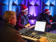 Musiker mit Weihnachtsmützen spielen Gitarre, Bass und Keyboard auf einer bunt beleuchteten Bühne.