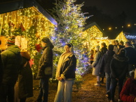 Besucher schlendern an glitzernden Weihnachtsbuden vorbei, umgeben von bunt beleuchteten Tannen.