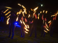 Eine Feuershow-Gruppe wirbelt synchron brennende Fackeln und zeichnet Muster in die Nachtluft.