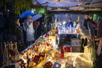in überdachter Kunsthandwerkstand bietet handgemachte Weihnachtsdeko an; Besucher mit Regenschirmen betrachten die ausgestellten Waren.