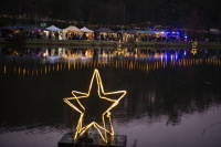 Impressionen vom Weihnachtsgarten 2025: Sonntag Leuchtende Sterne schwimmen auf dem Weiher und spiegeln sich im Wasser, dahinter Marktstände.