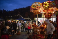 Ein Kinderkarussell dreht sich hell beleuchtet, umgeben von vielen Marktbesuchern in Winterkleidung.