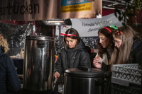 Frauen mit festlichen Haarreifen schenken warme Getränke an einem Stand aus.