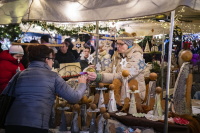 Eine Verkäuferin reicht einer Kundin handgefertigte Holzengel, umgeben von weihnachtlicher Deko.