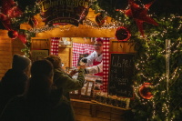 Eine Verkäuferin reicht Besuchern frisch gebackene Einhorn-Waffeln aus einem weihnachtlich dekorierten Holzstand heraus.