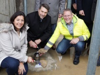 Drei Personen hocken in einem feuchten Raum und legen einen Grundstein für das Rohgebäude