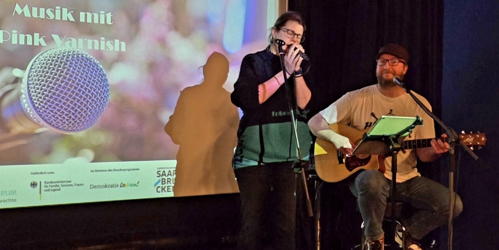 Sängerin und Gitarrist vor einer Leinwand
