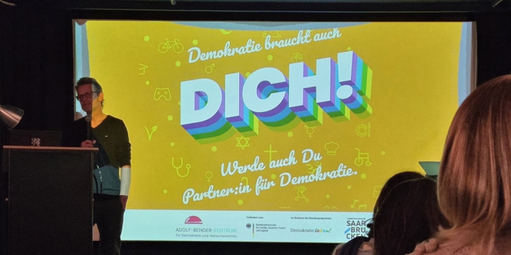 Mann vor einer Leinwand mit der Aufschrift Demokratie braucht dich