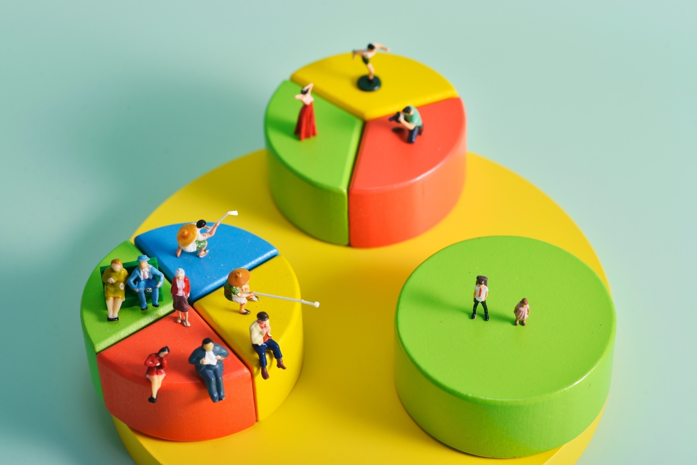 Miniaturen von Menschen, die verschiedene Aktivitäten ausführen, auf Bauklötzchen, die wie Kreisdiagramme aussitzen