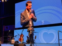 Ein Mann auf einer Bühne mit ihm nochmal auf einer großen Videoleinwand