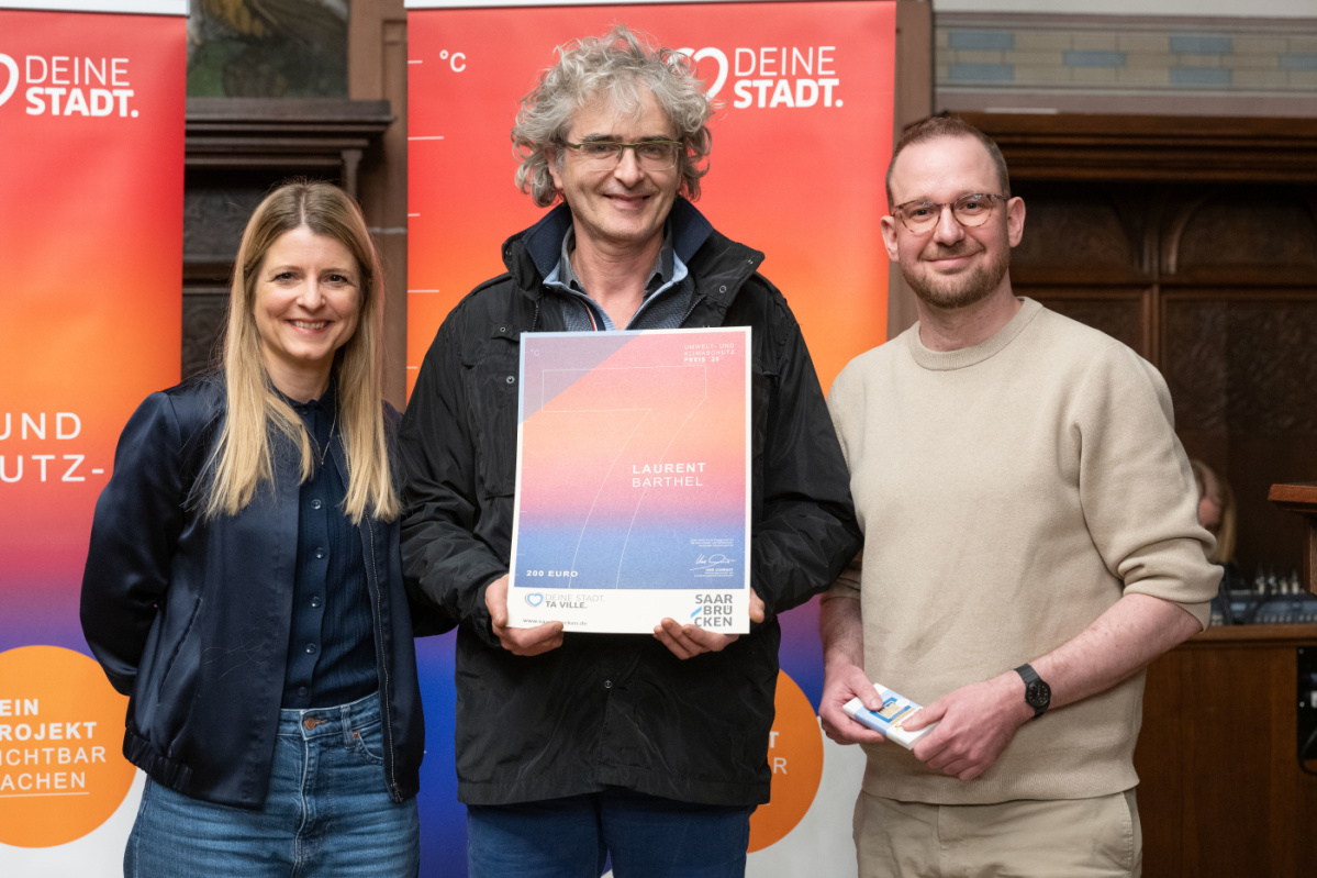 Preisträger hält Urkunde in Kamera und lächelt