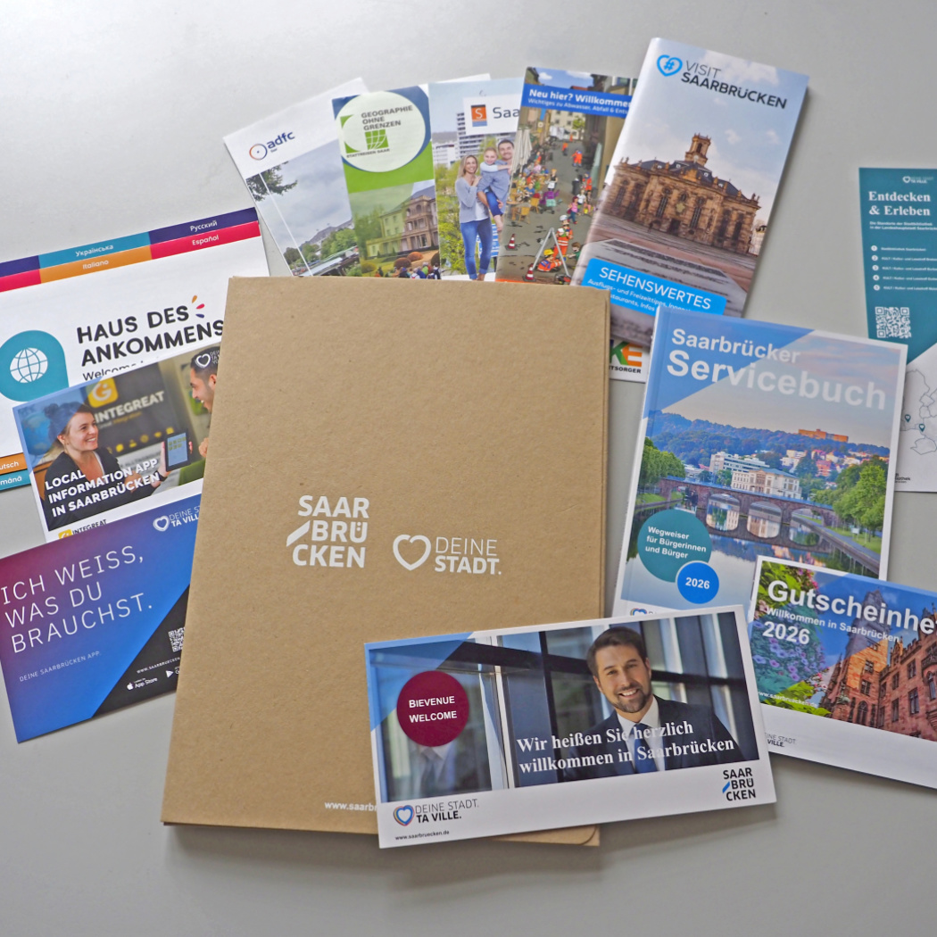 Braune Papiermappe mit Aufschrift Landeshauptstadt Saarbrücken, daneben Gutscheine und Informationsbroschüren.
