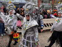 Drei kostümierte Frauen in silbernen Weltraum-Outfits mit großen glitzernden Kopfbedeckungen laufen am Straßenrand entlang.