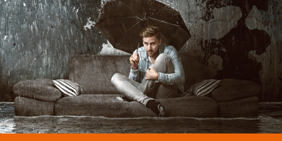 Slider Hochwasser und Starkregenvorsorge Symbolbild - Mann sitzt mitten im Hochwasser auf Sofa mit offenem Regenschirm