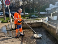 Ein Mann mit orange-blauer Arbeitskleidung reinigt mit einem Flächenreiniger eine gepflasterte Fläche