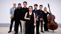 Sieben Musiker:innen mit Instrumenten und Mikrofonen in der Hand vor weißem Hintergrund