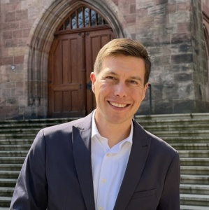 Ein Mann im Jackett steht vor einem großen, alten Gebäude
