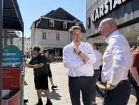 Zwei Männer stehen bei einer Veranstaltung in der Innenstadt im Gespräch. Im Hintergrund sind Infostände und weitere Personen.