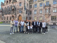 Eine größere Gruppe mit Erwachsenen und zwei Kindern steht für ein gemeinsames Foto vor einem historischen Gebäude.