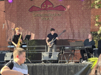 Auf der Bühne spielen drei Musiker Jazz: Einer spielt Bass, einer Saxofon und einer Keyboard.