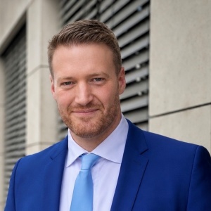 ein Mann in einem blauen Anzug mit Krawatte lächelt in die Kamera