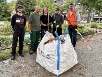 Fünf Personen stehen mit Rechen und Besen hinter einem großen, mit gesammelten Abfällen gefüllten Sack.