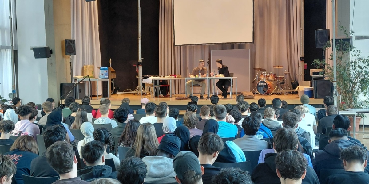 Viele Schüler hören einer Diskussion auf einem Podium zu